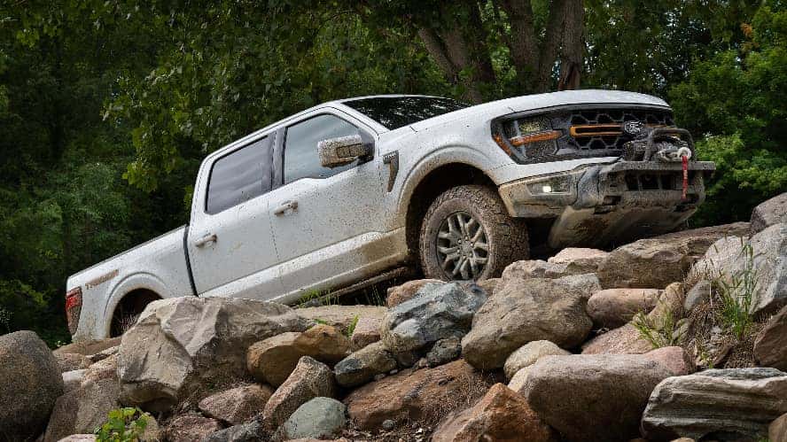 A silver Ford F-150 in profile driving over rocks.