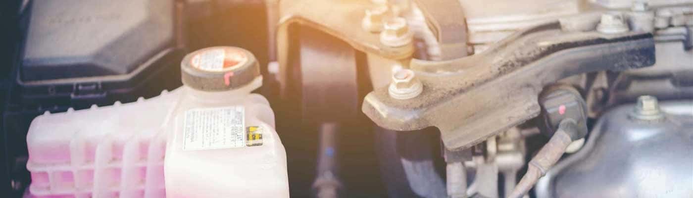 Close up view of a bottle of coolant next to an engine