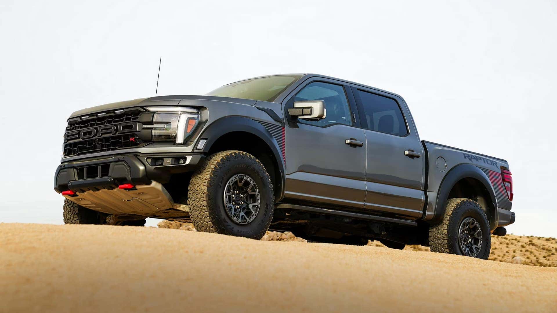 2026 Ford F-150 Raptor parked on sandy terrain, highlighting aggressive off-road styling, wide stance, and rugged suspension.
