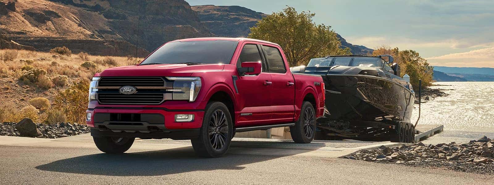 2026 Ford F-150 pickup truck towing a large boat on a trailer near a lakeside road, showcasing full-size truck capability and exterior design.