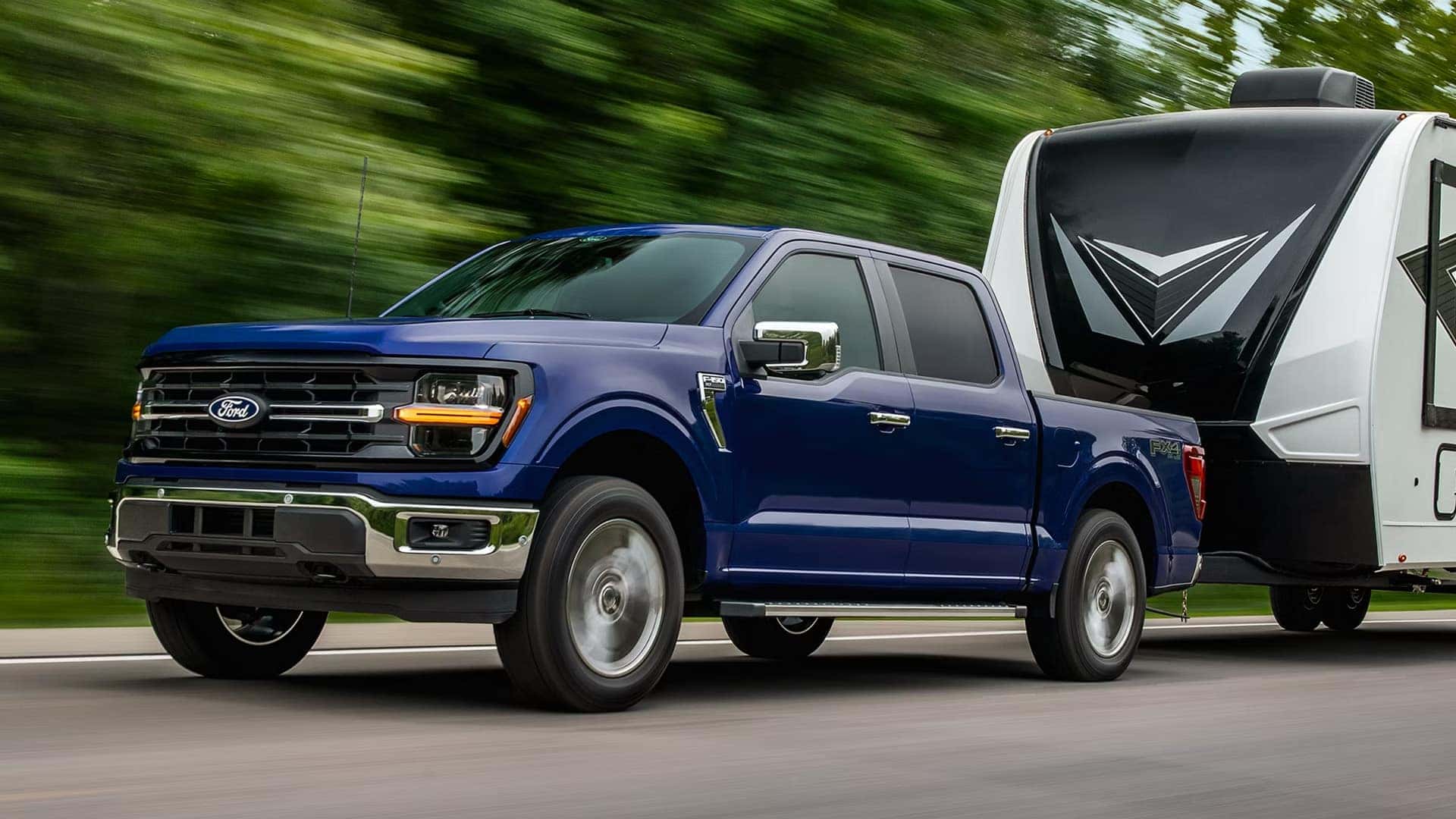 Blue 2026 Ford F-150 towing a travel trailer on the highway, demonstrating towing capability and on-road stability.