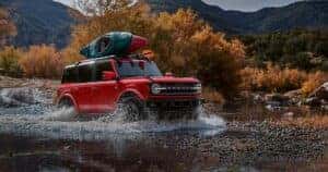 Red Ford Bronco driving through water in the mountains