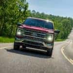 A red 2021 Ford F-150 is shown from the front driving down the highway after leaving a used Ford truck dealership.