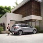 A silver 2013 Ford Escape is shown parked in a the driveway of a modern house.