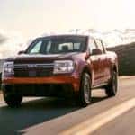 A red 2022 Ford Maverick Lariat is shown driving down a sunny road after visiting a Ford Maverick dealership.