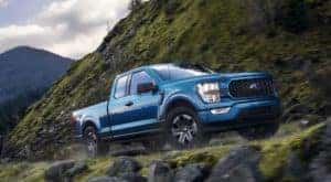 A blue 2021 Ford F-150 is shown from the side driving on a mountain road.