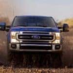 A blue 2022 Ford F-250 Super Duty Lariat is shown from the front driving through a mud puddle.