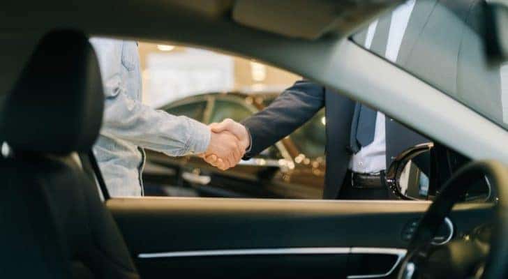 A salesman and car owner are shown shaking hands.