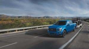 A blue 2020 Ford F-150 XLT is shown towing a boat after visiting a Certified Pre-Owned Ford F-150 dealership.