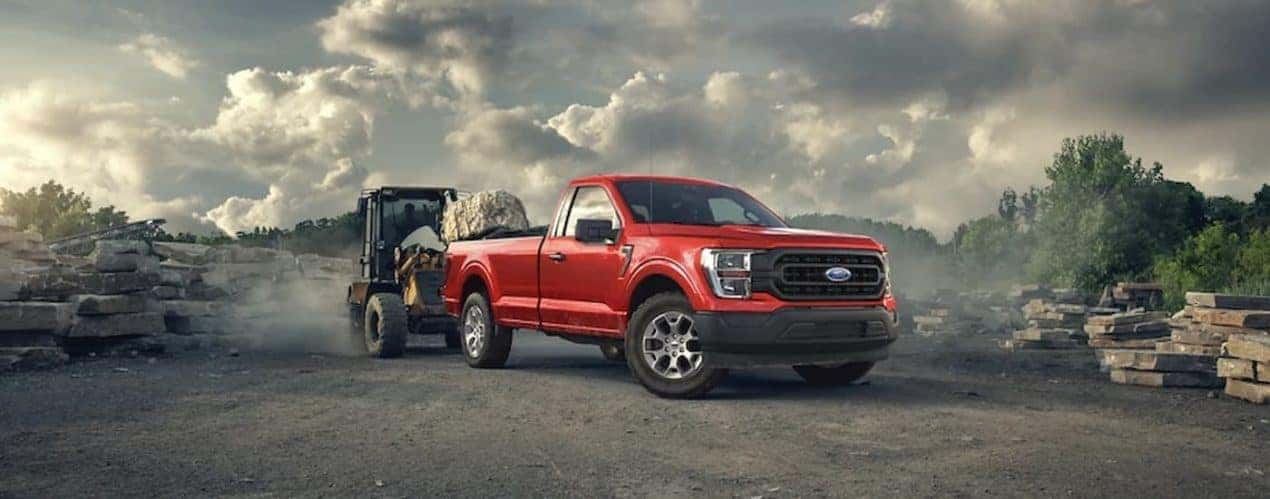 A red 2022 Ford F-150 XL is shown towing heavy machinery at a construction site.