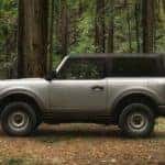 A silver 2021 Ford Bronco is shown from the side parked in the woods.